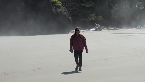 Mujer-Con-Chaqueta-Roja-Caminando-En-La-Niebla-Y-La-Neblina-En-La-Playa-Con-Formaciones-Rocosas-En-El-Fondo