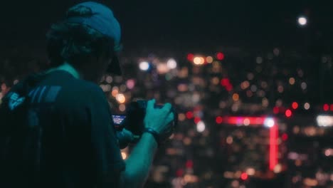 young adult sitting on ledge of skyscraper uses his camera to record downtown los angeles-1