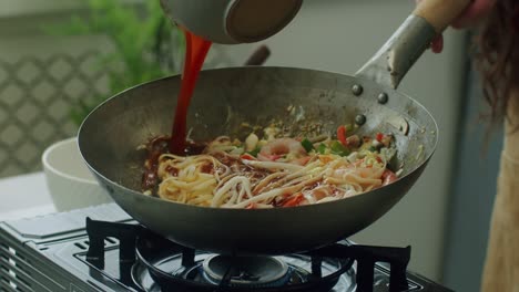 woman pouring broth into pan with wok noodles