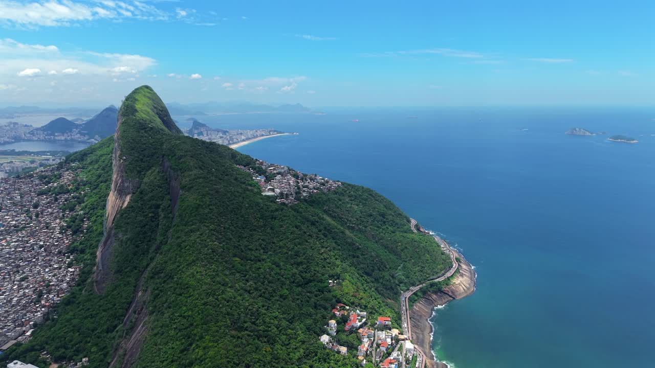Il picco del Morro Dois Irmãos domina il quartiere collinare di Rocinha, affacciato sulla costa atlantica a Rio de Janeiro, Brasile, mostrando un denso insediamento urbano che si fonde con la foresta tropicale, inquadratura aerea in avvicinamento