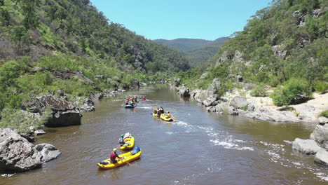 aerial: rafters below river rapid in sunny rock canyon in australia