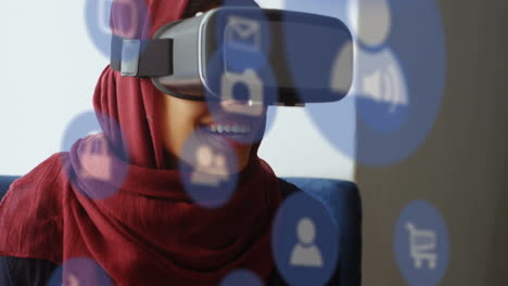 multiple digital icons floating against businesswoman in hijab wearing vr headset at office