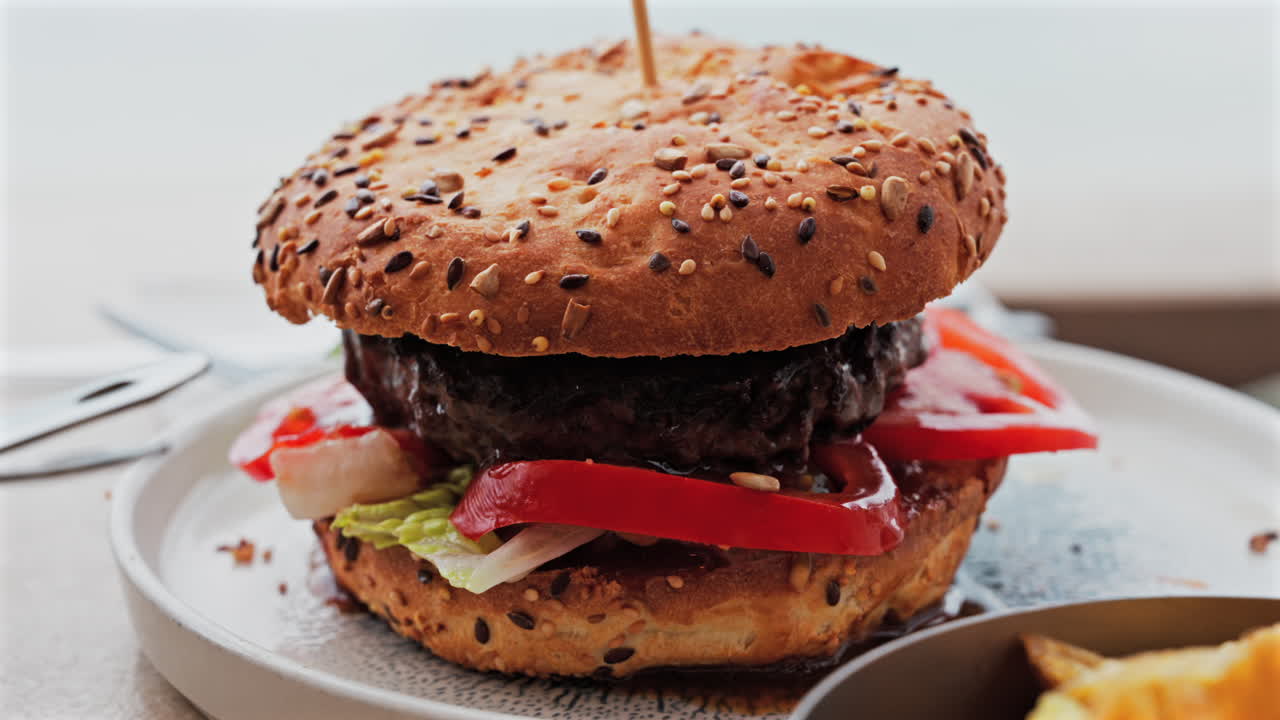 Close up of a hamburger on a white plate near french fries on a table at a restaurant