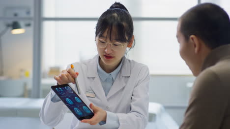 asian female doctor showing ct scan on tablet to patient