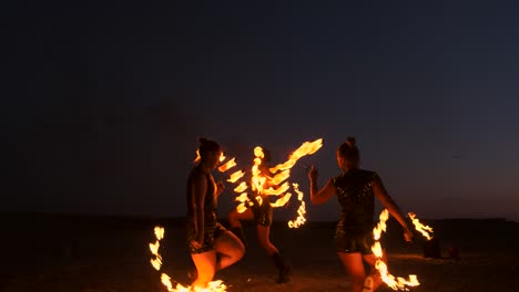 professional artists show a fire show at a summer festival on the sand in slow motion. fourth person acrobats from circus work with fire at night on the beach.