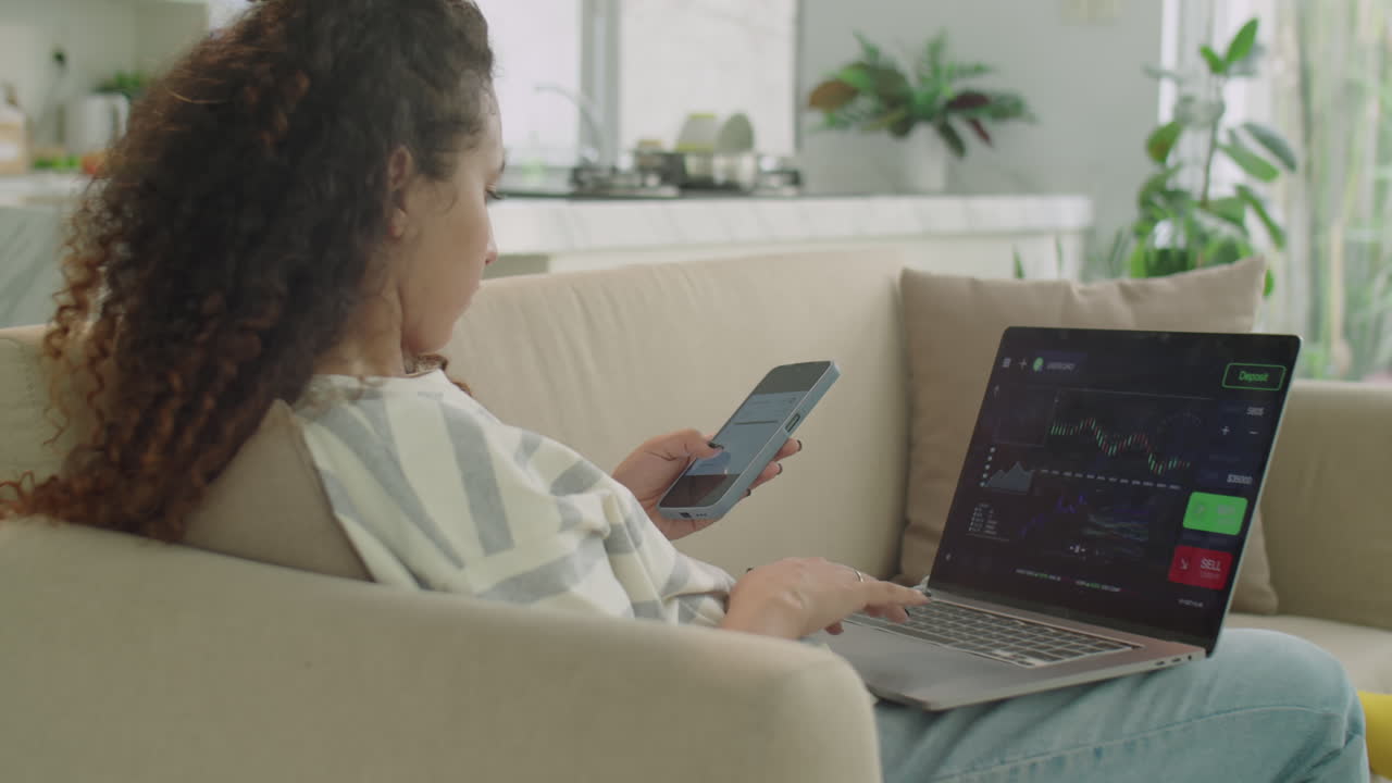 Young Girl Using Laptop and Phone while Trading Online at Home