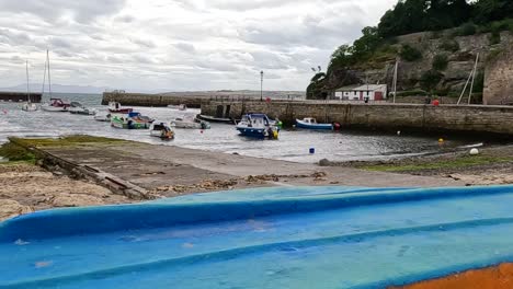 View of boats docked by a harbor wall with a vibrant blue rail in the foreground.