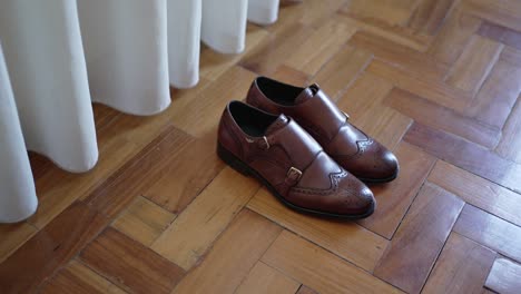 elegant brown leather groom shoes placed on wooden floor near white curtain