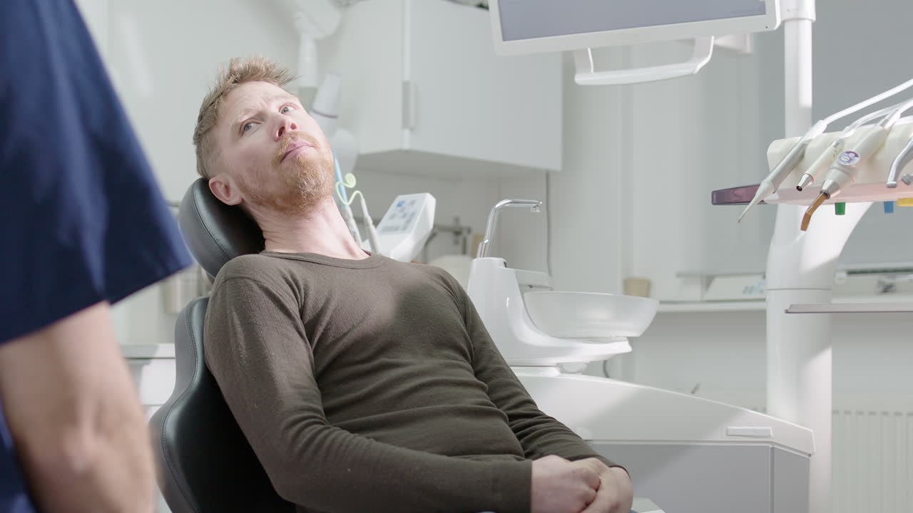 Dentist speaks to male dental patient sitting in reclined chair. Slider