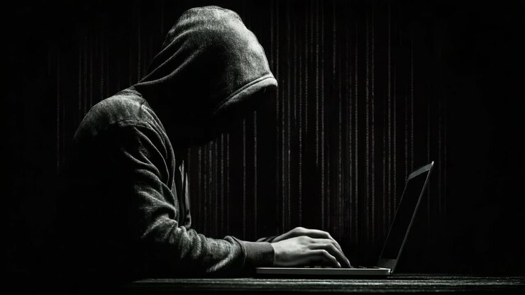 Una figura misteriosa con una felpa con cappuccio interagisce con un laptop, circondata da codice digitale a matrice che simboleggia l'intrigo dei mondi della cybersecurity e dell'hacking.