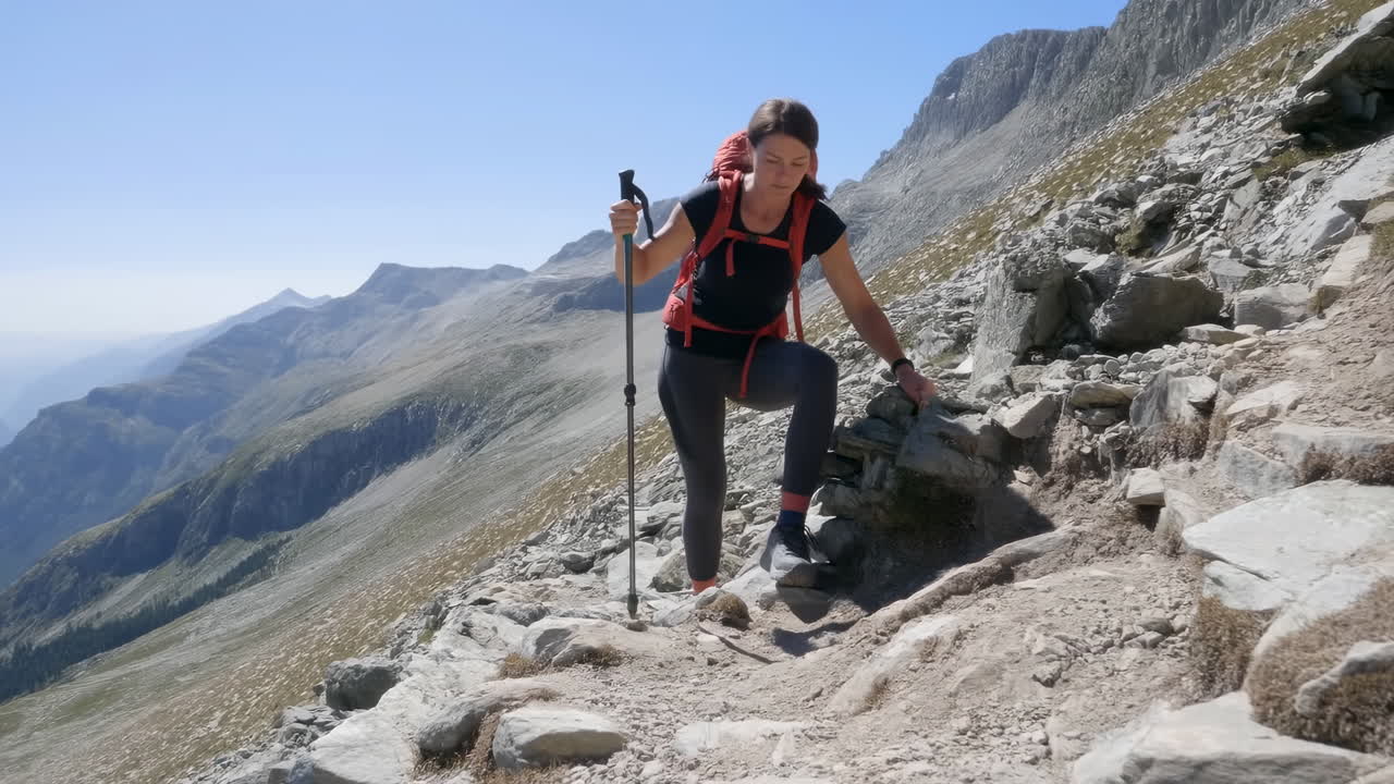 Mujer descendiendo por un sendero de montaña rocoso con una mochila