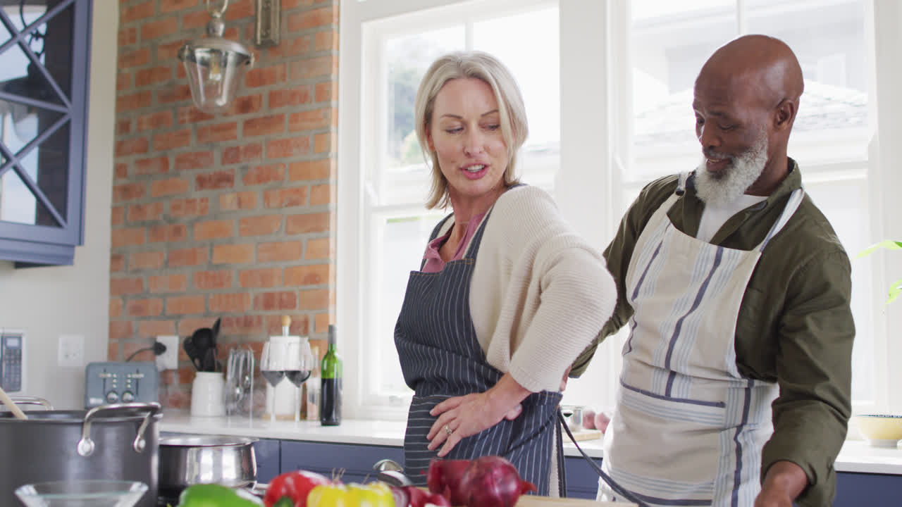 un anciano afroamericano atando un delantal a su esposa en la cocina de su casa.