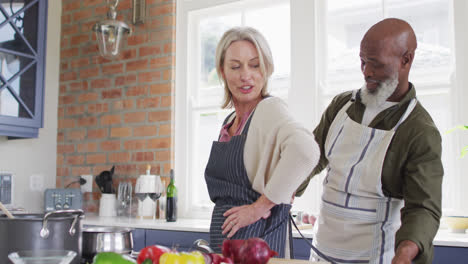 African-american-senior-man-tying-apron-to-his-wife-in-the-kitchen-at-home