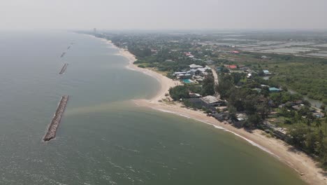 4k aerial drone footage along the coastal area of ban laem in phetchaburi, thailand with stone wall breakwater barriers.
