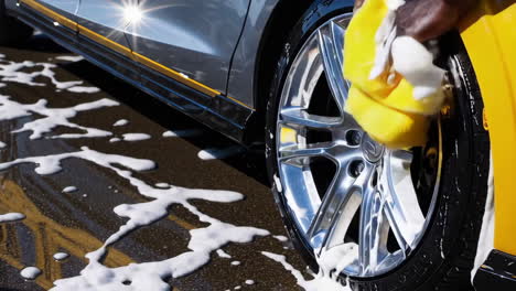 person washing a car wheel with soap and a sponge