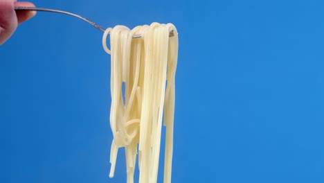 mano masculina sosteniendo un tenedor con espagueti de pasta hervida.