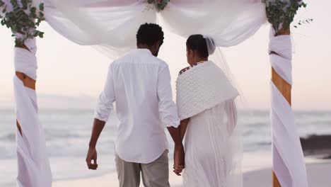 african american couple in love getting married, holding hands and walking on the beach