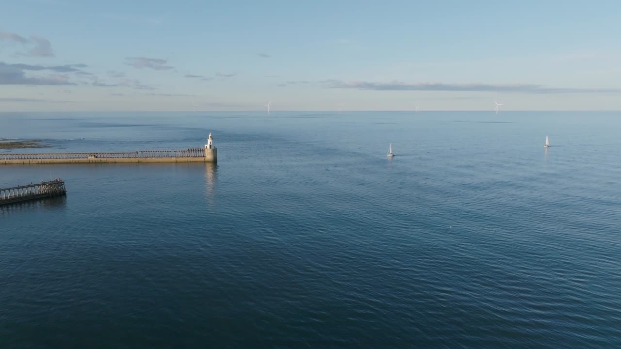 Clip con drone di due barche che navigano verso un porto illuminato dal sole con faro.