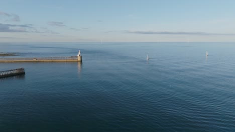 drone clip of two boats sailing towards sunlit harbour with lighthouse