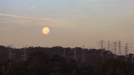 luna llena sentada sobre líneas eléctricas recortadas sobre el suministro de energía a las áreas suburbanas circundantes