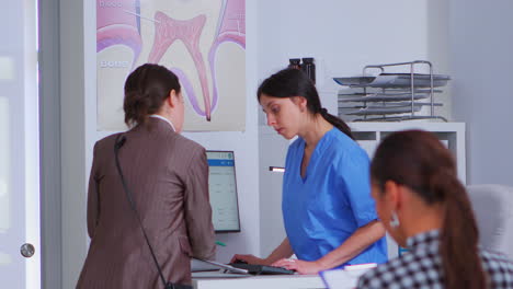 Asistente-Dental-Haciendo-Citas-Mientras-La-Mujer-Pide-Ayuda