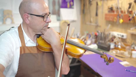 Luthier-master-playing-violin-in-workshop