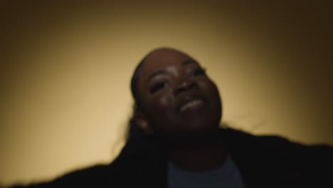 head and shoulders studio portrait shot of young woman dancing in spotlight against yellow background 5