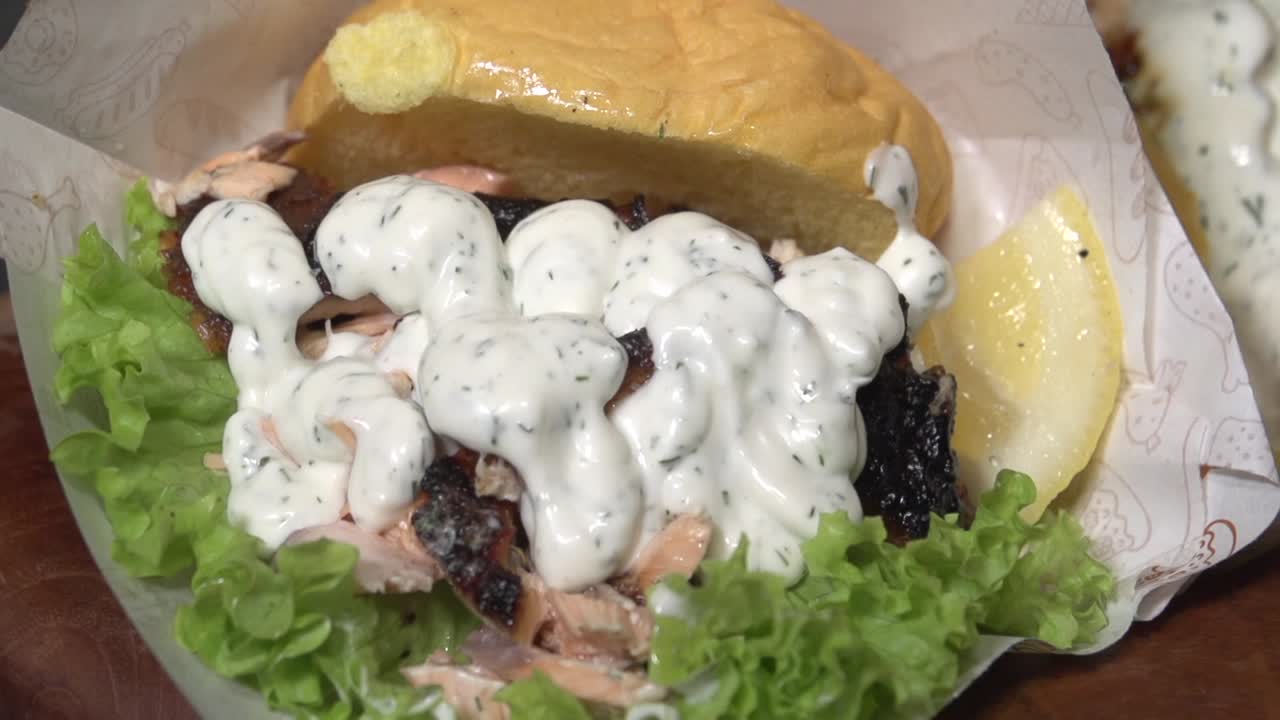 Salmon sandwich in a potato bun with lettuce and a wedge of lemon smothered in sauce