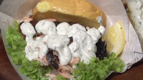 salmon sandwich in a potato bun with lettuce and a wedge of lemon smothered in sauce