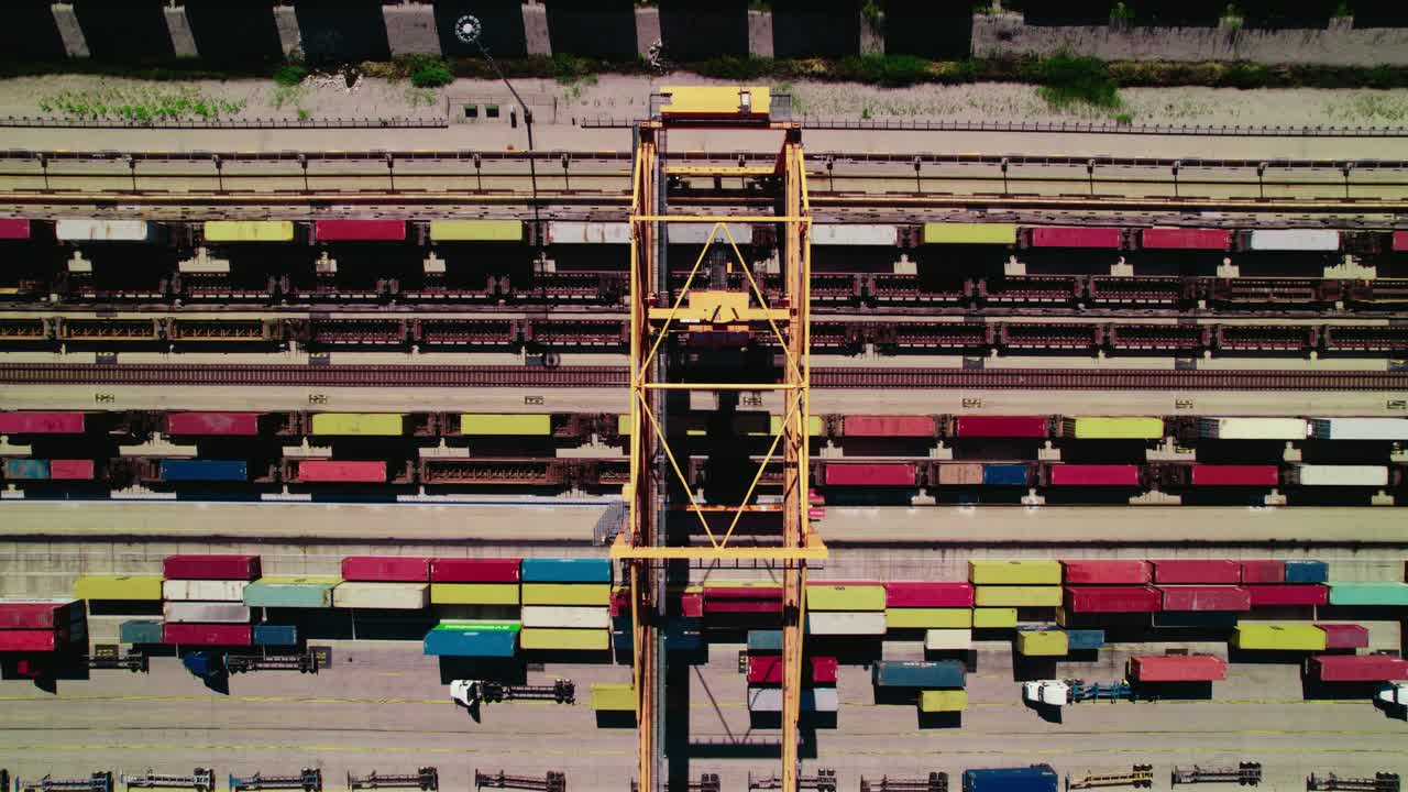 Aerial perspective centered on a towering yellow gantry crane, overlooking a vibrant tapestry of colorful shipping containers and multiple rail tracks