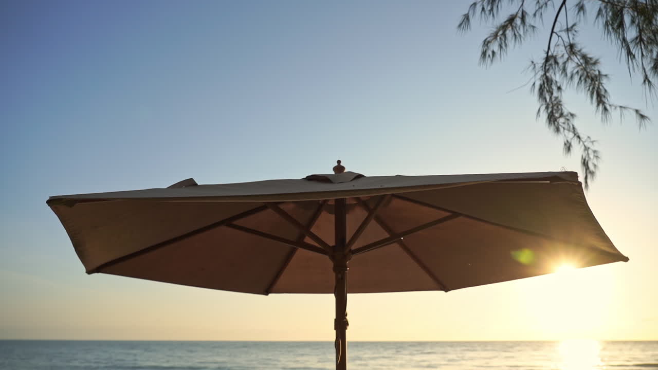 Low angle view of an umbrella and the ocean during sunset. Panning shot