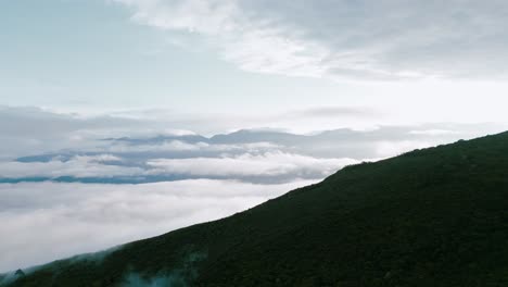Soar-above-the-clouds-in-this-stunning-drone-footage,-as-majestic-mountain-peaks-rise-in-the-background,-accentuating-the-captivating-Yungas-cloud-forest-below