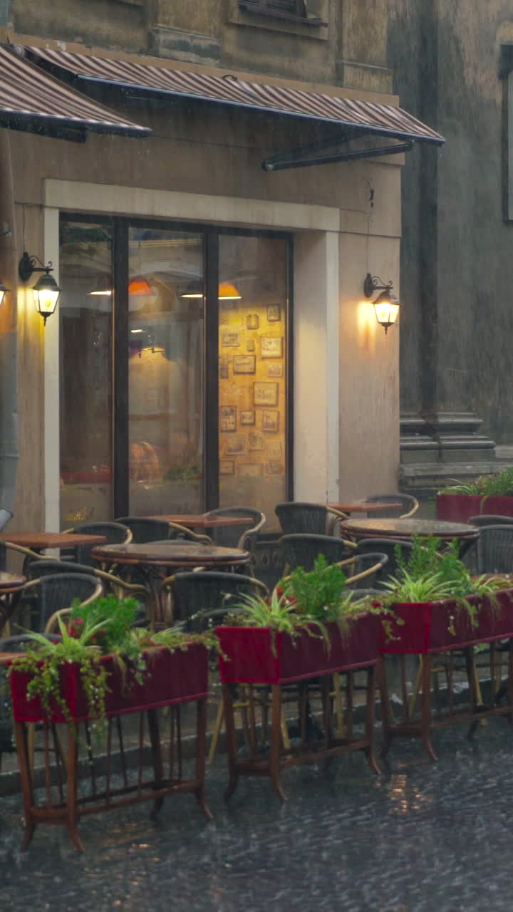 view on a wet summer terrace of the cafe with flowers, tables and chairs in the street in rainy weather. It's raining cats and dogs Vertical video