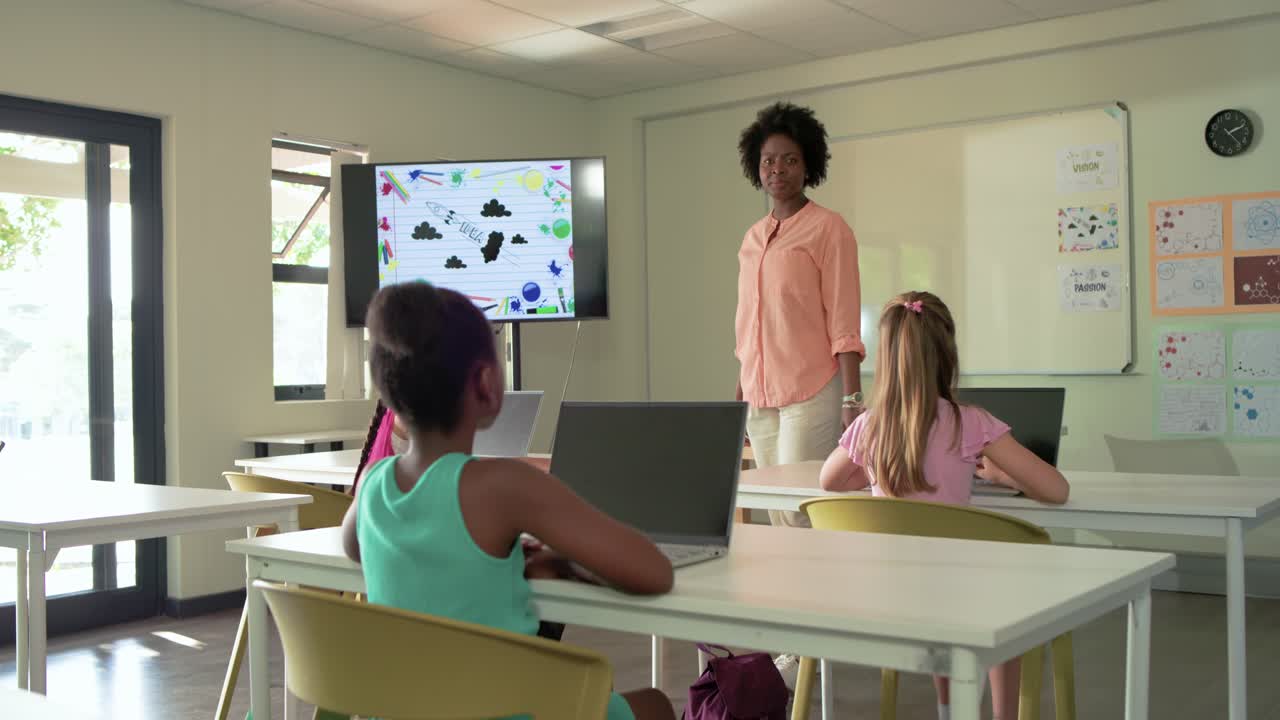 Bambino afroamericano in classe che usa un laptop dopo che un compagno ha alzato la mano, alza la mano e risponde