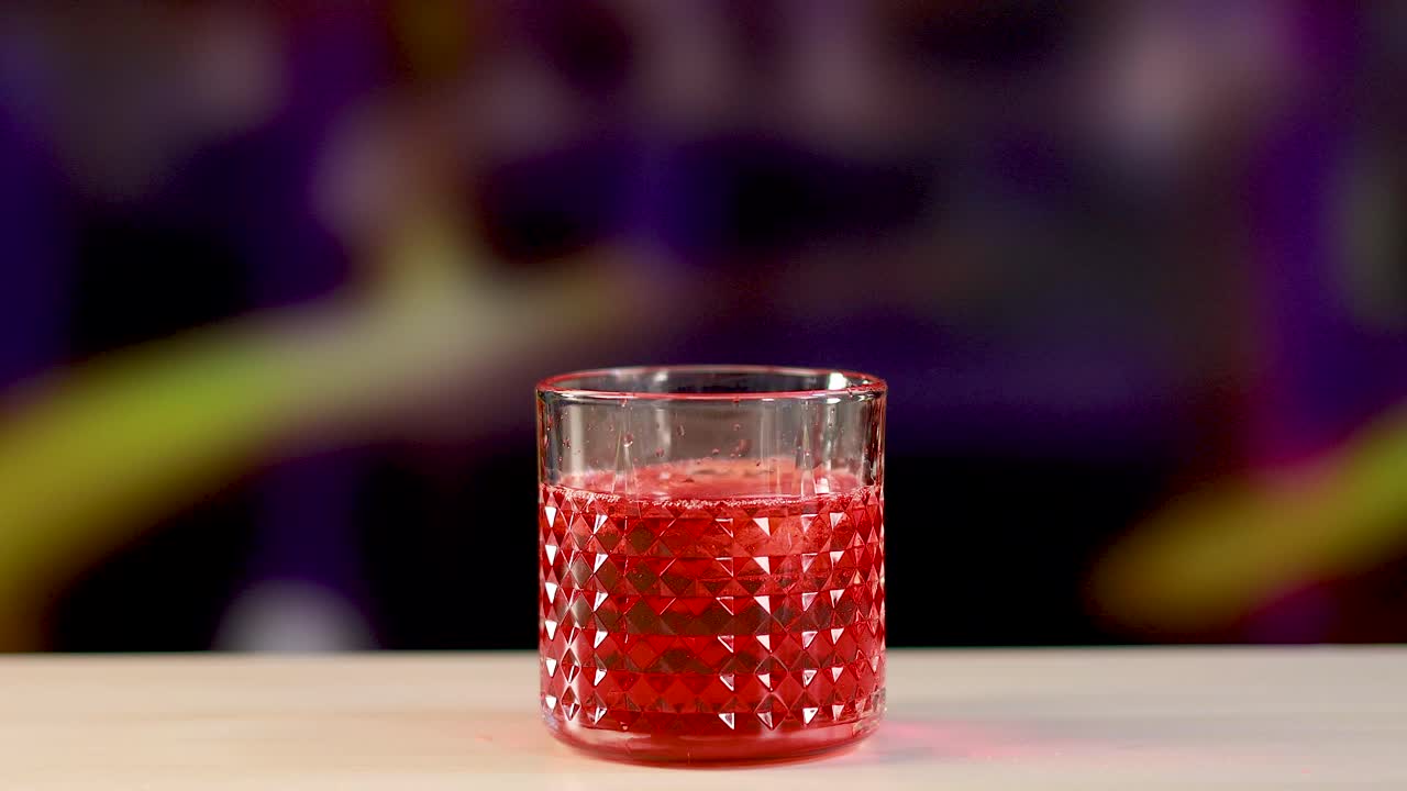Red liquid pours into a textured glass against a colorful background, creating a vibrant and dynamic scene
