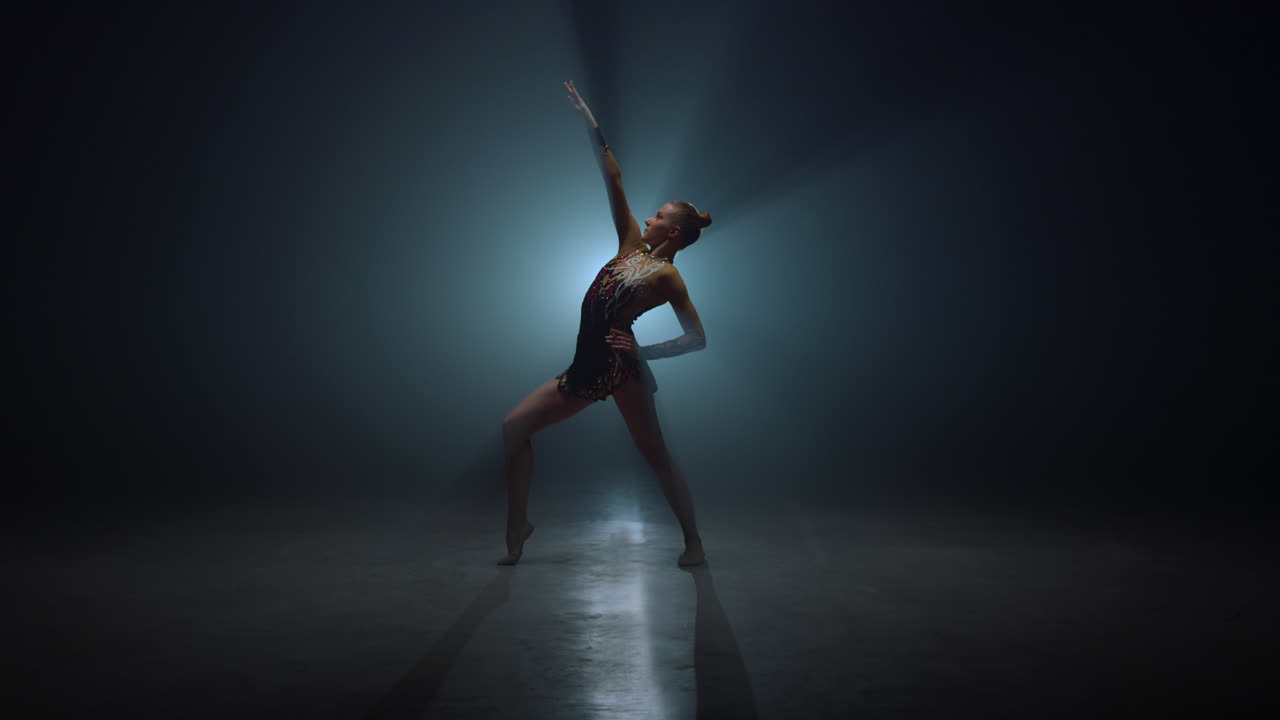 Graceful sportswoman posing indoors. Slim gymnast bending in dark space.