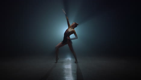 graceful sportswoman posing indoors. slim gymnast bending in dark space.