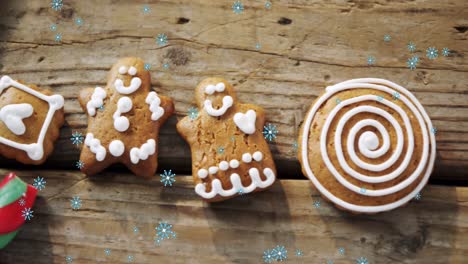 copos de nieve cayendo contra galletas de pan de jengibre hombre y caña de caramelo en la superficie de madera
