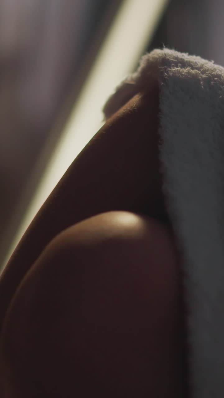 mujer con las piernas cruzadas cubiertas con un borde de bata de terry en una habitación de hotel turística débilmente iluminada. mujer se relaja mirando por la ventana panorámica del apartamento sentada en un sillón