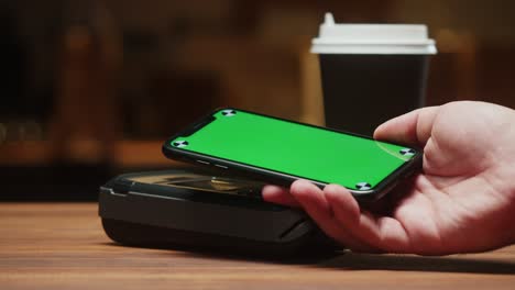 paying by smartphone with chroma green screen close-up. cashless shopping in restaurant or cafe. buying coffee using touch-free and contactless payment concept. nfc technology and bank terminal.