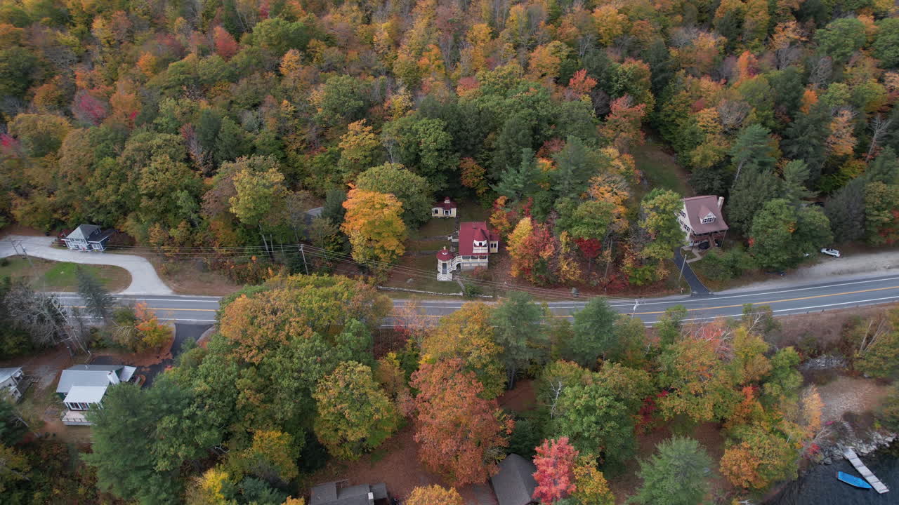 vista aérea del tráfico en la carretera costera por el lago sunapee, colorido follaje de otoño y casas frente al lago, disparo de drones