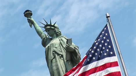 Una-Vista-Inclinada-De-Una-Bandera-Estadounidense-Mientras-Ondea-Frente-A-La-Estatua-De-La-Libertad