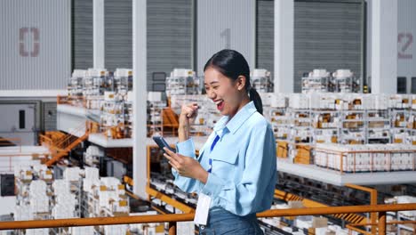 side view of happy asian business woman celebrating using mobile phone in the warehouse