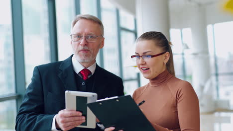 office workers speaking happily. mature businessman in suit talking to his young secretary about new project in a modern company.