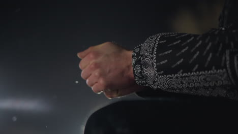 hand view of man rubbing hands together to stay warm in cold night air, snow flares gently falling in background, soft glow from bokeh light accentuates winter chill and layered clothing details