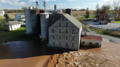 aerial of flooded grain mill, silos, elevators beside muddy river on sunny day