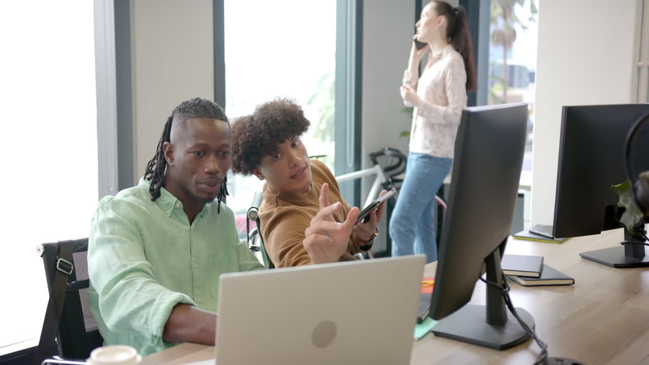 Collaborating on project, two colleagues using laptop and desktop in modern office