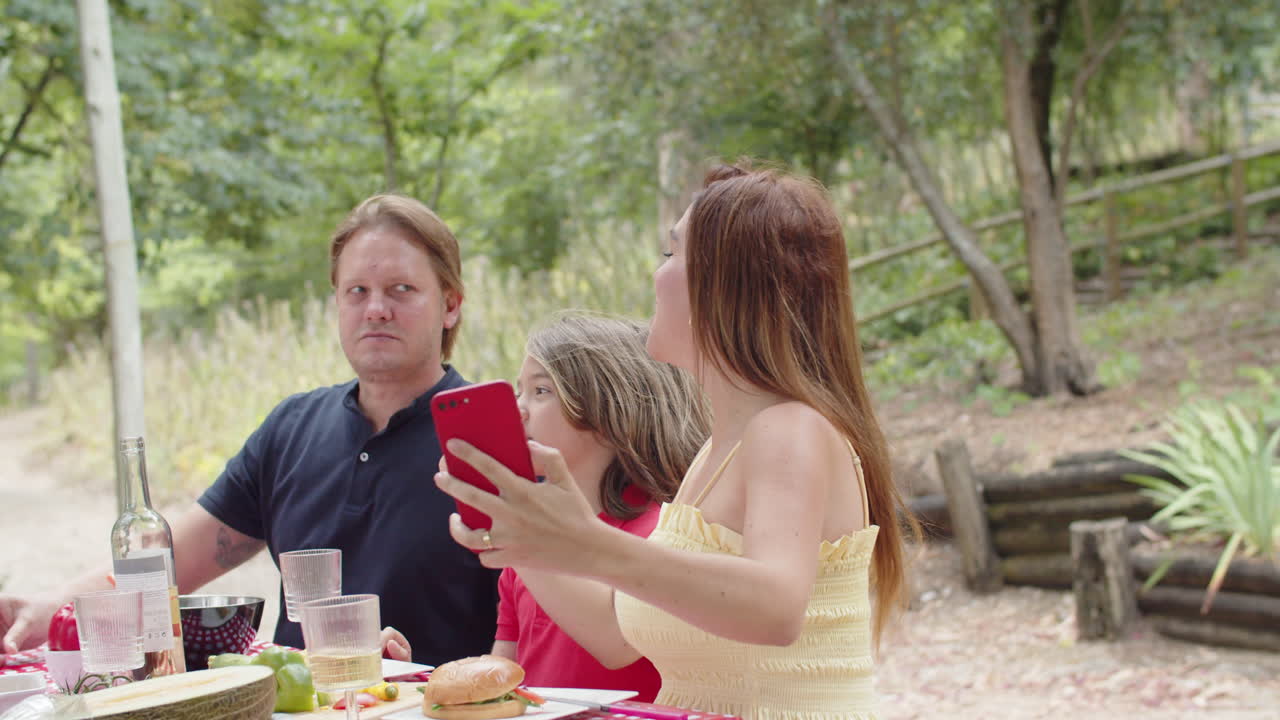 mujer caucásica feliz tomando una foto selfie con su familia durante un picnic en el bosque