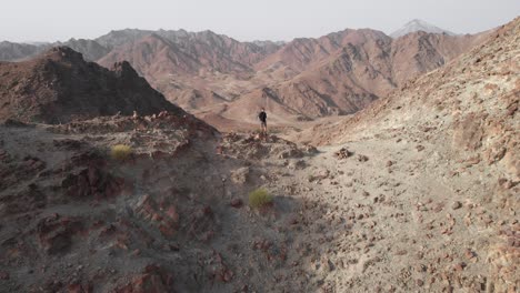 Revealing-aerial-epic-shot-from-drone-of-an-young-male-standing-on-top-of-a-rocky-mountain-in-Hatta,-United-Arab-Emirates