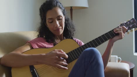 Glückliche-Frau-Mit-Gemischter-Abstammung,-Die-Auf-Dem-Sofa-Sitzt-Und-Gitarre-Spielt